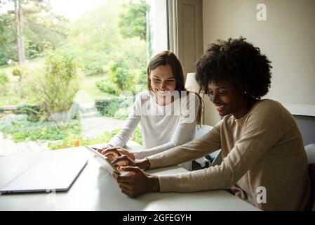 Smiling young women using digital tablet at home Stock Photo
