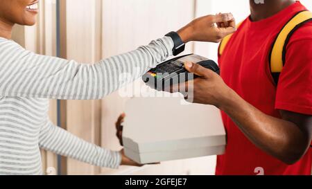Unrecognizable African Woman Paying Courier For Pizza Using Smartwatch Indoor Stock Photo