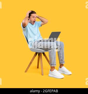 Surprised shocked guy using laptop sitting on chair Stock Photo
