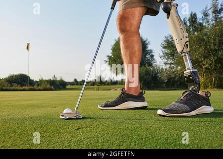 Professional golfer with prosthetic leg hitting with putter on golf ball during golfing. Concept of willpower of people with disabilities in sport Stock Photo