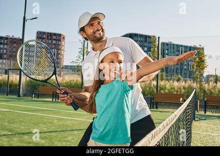 tennis lesson for a child. tennis coach teaches little girl to play tennis on grass court Stock Photo