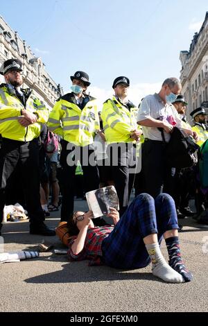 London, UK. 25th Aug 2021. A female protestor lies down and reads a book in front of a line of police as Extinction Rebellion protesters descend on Oxford Circus, where they blocked traffic with a giant pink table, danced peacefully and heard speeches, as climate demonstrations in London continue on August 25, 2021. Credit: Kieran Riley/Pathos Credit: One Up Top Editorial Images/Alamy Live News Stock Photo