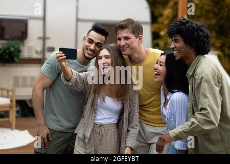 Happy multiracial friends taking selfie near their trailer, smiling and having fun together during autumn camping trip Stock Photo