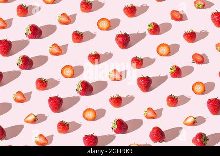 Colorful pattern of strawberries whole and cut on a pink background. View from above. Minimal concept of summer berries. Stock Photo