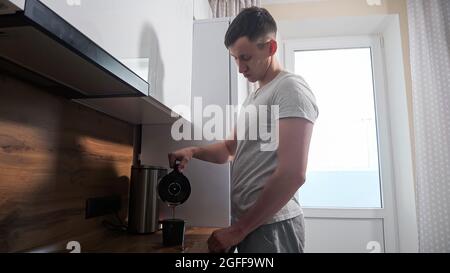 Sleepy man pours coffee from the coffee maker and accidentally spills it on the table Stock Photo