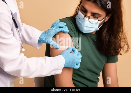 Nurse in workwear and gloves making vaccination for middle-eastern guy Stock Photo