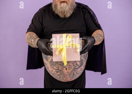 Plus size man on purple background closeup, focus on hands with gift box Stock Photo