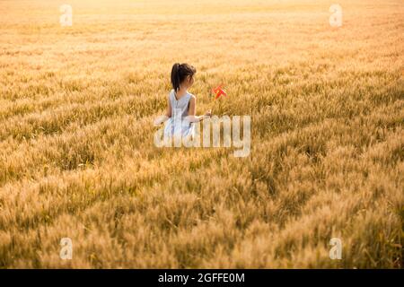 Little girl playing with paper windmill in wheat field Stock Photo