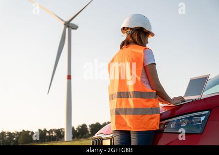 An windmill engineer supervises the work of the wind turbines on the laptop standing near the car. Generation of eco green electricity.  Stock Photo