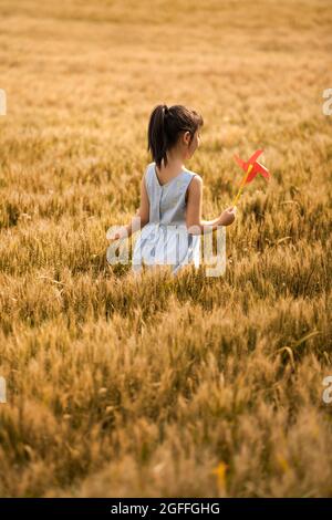 Little girl playing with paper windmill in wheat field Stock Photo