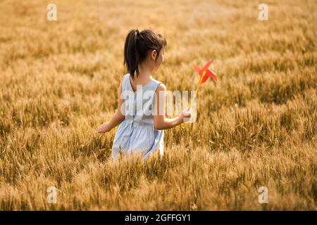 Little girl playing with paper windmill in wheat field Stock Photo