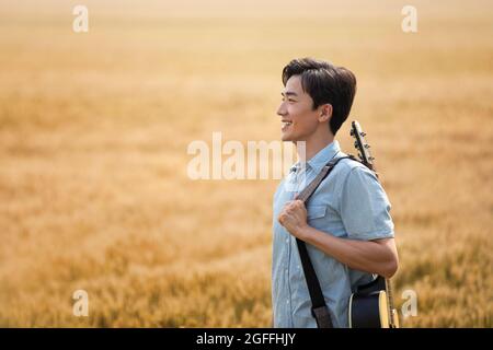 Happy young man with guitar in wheat field Stock Photo