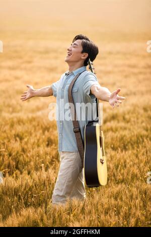 Happy young man with guitar in wheat field Stock Photo