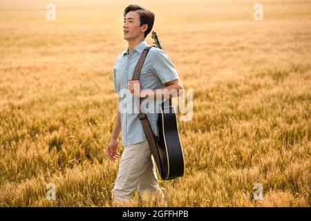 Happy young man with guitar in wheat field Stock Photo