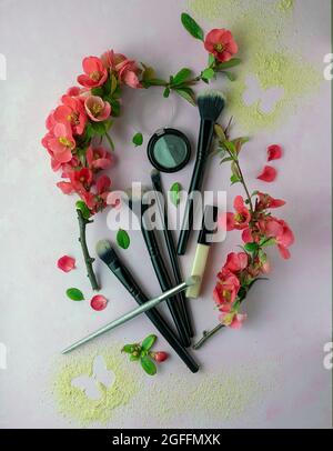 Cosmetic brushes and red spring flowers on a pastel pink background with powder butterflies. Makeup Accessories. Top view. Flat Lay. Stock Photo