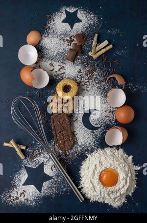 Ingredients for making cakes on a dark background. Flour, eggs, whisk, stars and the moon made of flour. Creative concept, top view flat lay. Stock Photo