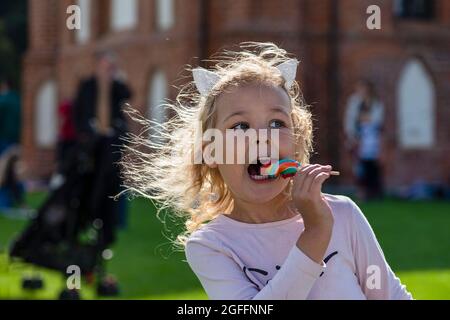 Girl eating colorful candy. A five year old girl in pink clothes is eating a colorful candy on a stick. Sunny summer day Stock Photo