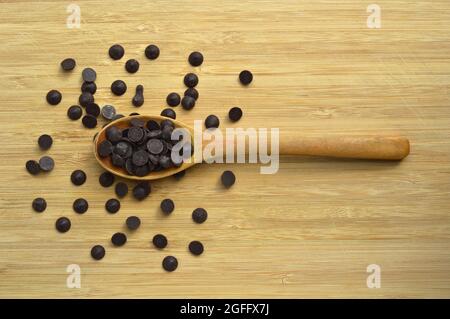 Delicious dark chocolate drops in wooden spoon, on cutting board Stock Photo