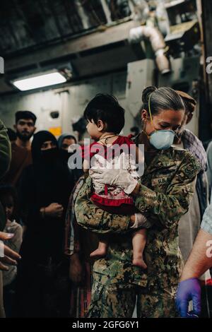 Sigonella, Italy. 22nd Aug, 2021. U.S. Navy Command Master Chief Anna Wood assists evacuees as they disembark from a U.S. Air Force C-17 Globemaster III aircraft after arrival at Naval Air Station Sigonella August 22, 2021 in Sigonella, Italy. NAS Sigonella is providing temporary lodging for evacuees from Afghanistan as part of Operation Allies Refuge. Credit: Planetpix/Alamy Live News Stock Photo