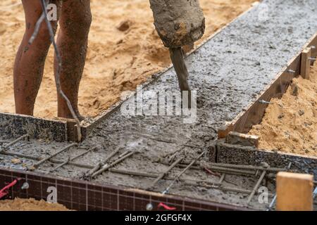 Pouring ready-mixed concrete in formwork with reinforcement. Wet cement pours to civil building foundation, close up. Stock Photo