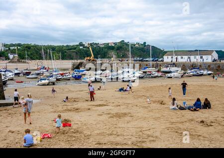 Families play on the beach left exposes at low tide at the back of Tenby Marina in Pembrokeshire, Wales. Boats are left beached on the sand. Stock Photo