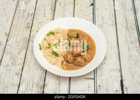 Portion of meatloaf in mushroom sauce garnished with white rice with chopped parsley on a white plate Stock Photo