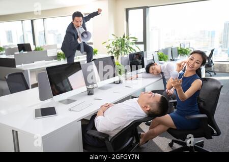 Angry manager yelling at employees through megaphone in office Stock Photo
