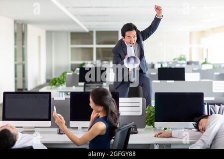 Angry manager yelling at employees through megaphone in office Stock Photo