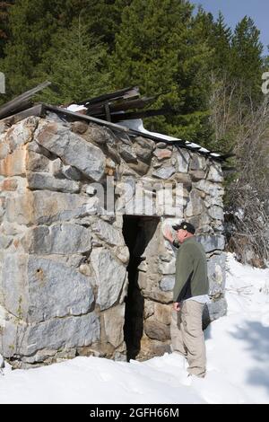 Visitor gives scale to the masonry vault, all that remains of the Hyde & Freychlag Bank, Granite Ghost Town State Park, MT. (MR) Stock Photo