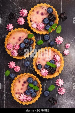 Four round shaped cheesecakes with fresh blackberries, blueberries, meringue and mint on a gray stone background. Stock Photo