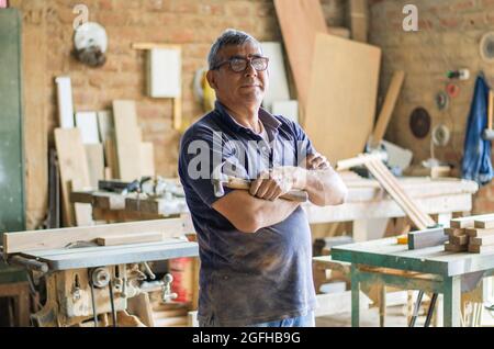 Elderly carpenter posing with crossed arms in his workshop Stock Photo