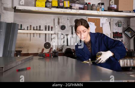 Woman apprentice measures metal sheet with tape measure Stock Photo