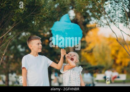 Happy children boy and girl eating blue cotton candy outdoors. Stock Photo