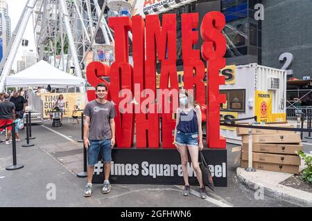 New York, United States. 25th Aug, 2021. People pose for a photo in front of the Times Square wheel sign on opening day in Times Square, New York City.The 110-foot Times Square Ferris Wheel, located on Broadway between 47th and 48th street, will be open until September 14th, 2021. Credit: SOPA Images Limited/Alamy Live News Stock Photo