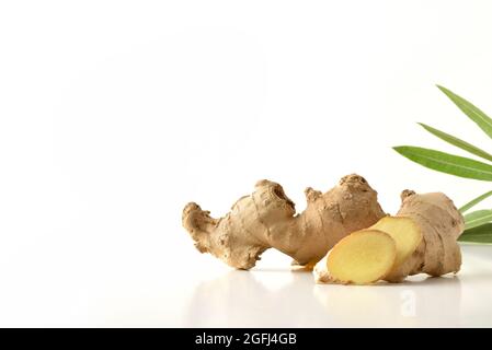 Ginger root with sliced portions and leaves behind with white isolated background reflected on white table Stock Photo
