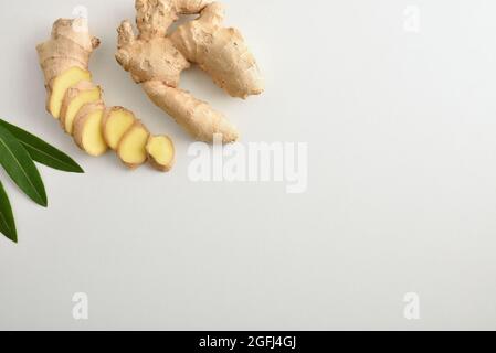 Fresh ginger root with sliced portions on white table and leaves. Top view. Stock Photo