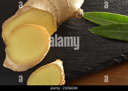 Ginger root slice on wooden cutting board on wooden table with leaves close up. Top view. Stock Photo