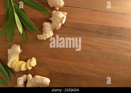 Ginger root as a product for healing purposes with sliced portions and leaves on wooden table. Top view. Stock Photo