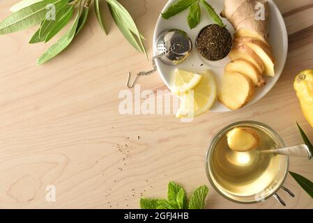 Cup of green tea with ginger lemon and mint on wooden table with sliced root and metal strainer filled with tea on white dish and leaves on wooden tab Stock Photo