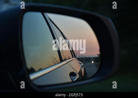 Soft focus view from car window with road reflection into side mirror. Dusky blurred reflection while driving in evening. Road trip in blue dusk Stock Photo