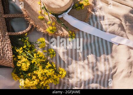 overhead top view of straw hat with bag on blanket bouquet of yellow rapeseed flowers Stock Photo