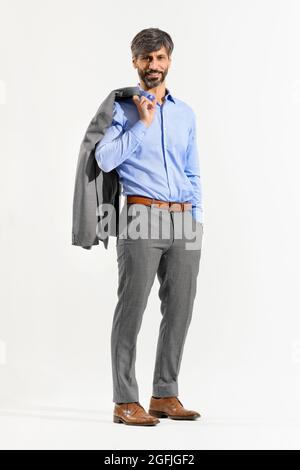 Attractive relaxed confident stylish 50 year old businessman in a suit standing with hand in pocket and jacket slung over his shoulder smiling at the Stock Photo