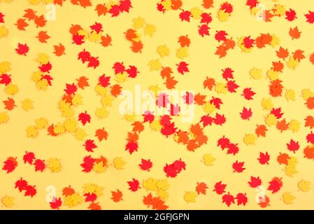 Multicolored falling maple leaves, paper confetti on a yellow background. Stock Photo