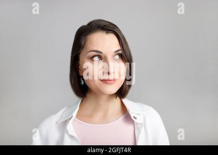 High key portrait of smiling young brunette multiethnic woman in pink tank and white shirt looking at top corner. Stock Photo