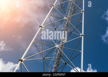 Bottom perspective pov of modern metal steel mobile 5g network wireless telecom tower against clear blue sky background on bright day. Microwave Stock Photo
