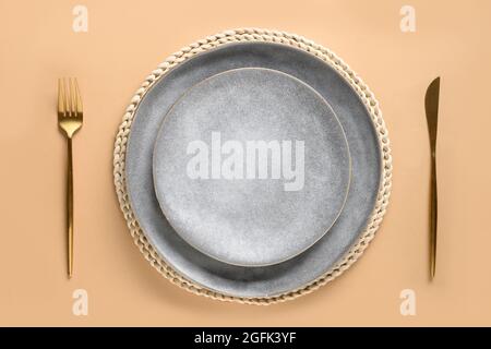 Elegance table setting with empty gray plate with golden cutlery as mockup on beige autumn table. Top view. Stock Photo