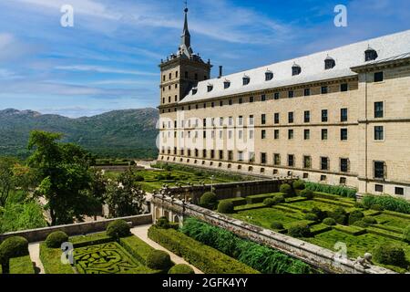 View of the San Lorenzo de el Escorial monastery in Madrid, with gardens in the foreground and blue sky with light white clouds.