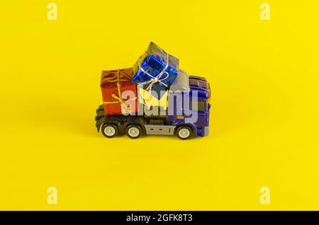 Toy truck carrying boxes of gifts. Blue car with a blue and red box. Gift delivery. Yellow background. Stock Photo