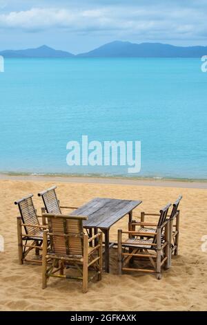 Wooden bamboo furniture, table and five chairs around on sand beach with blue sea water background in Koh Samui island, Thailand Stock Photo