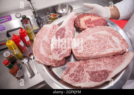 Close up of a plate full of raw marbled beef steaks in the hands of professional chef Stock Photo